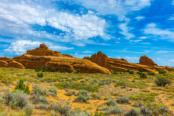 A row of rounded orange sandstone mesas and domes rises above sagebrush flats under dramatic blue sky with white clouds, Arches National Park, Utah. © ZL Visuals