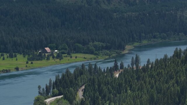 Aerial of Pend Oreille river in forested valley in Ruby Washington in summer with open grassy areas and rural buildings