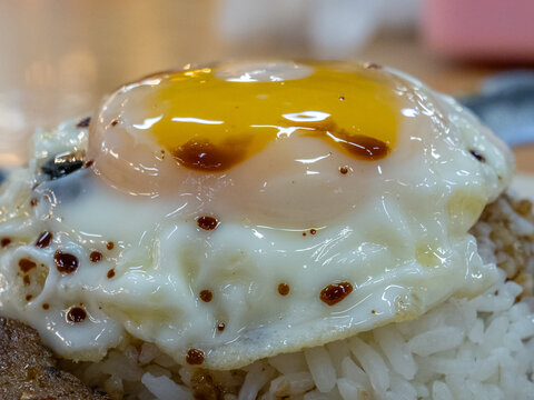 Macro shot of a sunny-side-up fried egg on rice, drizzled with soy sauce.
