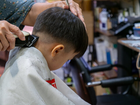 A young boy receives a neat fade haircut from a barber using clippers, captured in a close-up shot at a cozy barbershop.