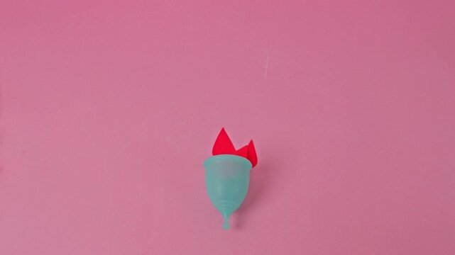 Video Stop Motion Blue menstrual cup with paper blood drops on pink background