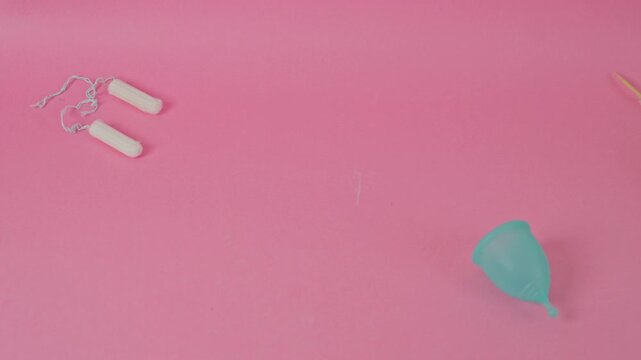 Feminine hygiene choice between tampons and reusable cup on pink