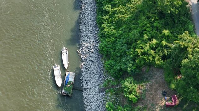 Small boats moored along the Po River beside a riprap embankment near Castelvetro Piacentino, Piacenza, Emilia-Romagna, Italy, bordered by riparian woodland, drone top down