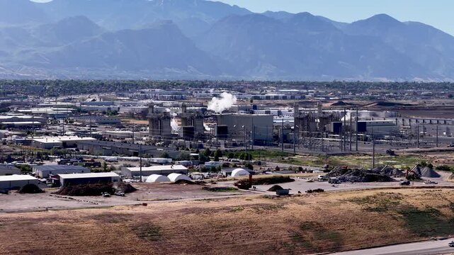 Pipe coating facility at Vineyard near Lindon, Utah, USA, features coating lines, curing units and cooling steam with the Wasatch Range rising behind, orbiting drone estabishing shot.