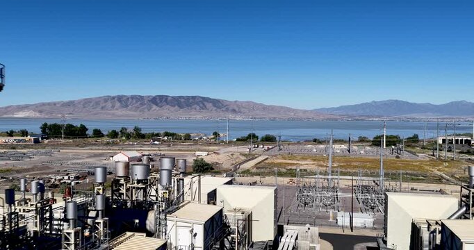 Large process manufacturing facility beside Utah Lake in Lindon, Utah, smokestacks, industrial piping, utility infrastructure and adjacent construction near Utah Lake Mountains, drone pullback reveal