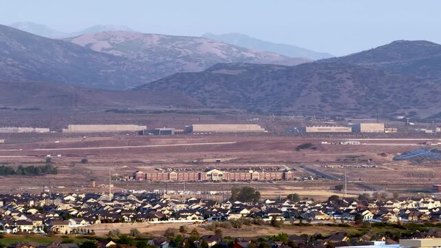 The Utah Data Center with a Lehi suburb in the foreground and the Oquirrh Mountains in the background on a hazy day - sliding aerial zoomed in view
