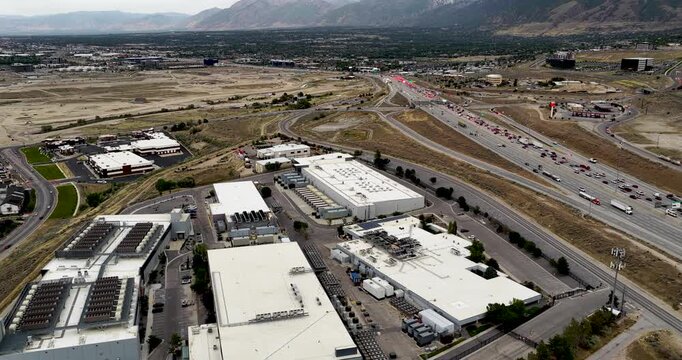 Drone video captures a sweeping aerial panorama of a modern data center in Bluffdale, Utah beside I-15 highway, with Wasatch Front mountains and Salt Lake Valley at daytime.