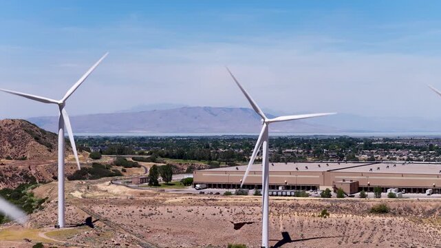 Windward Engineering wind turbines with three-blade rotors and nacelles near US-89, Spanish Fork, Utah County, Utah, USA, overlooking Utah Valley beneath the Wasatch Range, drone slow pullback