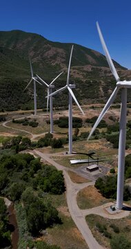 Vertical Windward Engineering wind turbines with three-blade rotors, nacelles and tubular steel towers near Spanish Fork, Utah County, Utah, USA, below the Wasatch Range, drone forward flyover