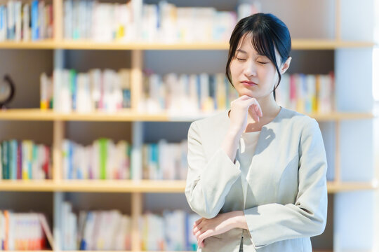 本棚の前に立つ困った表情の女性　作家　小説家　エッセイスト