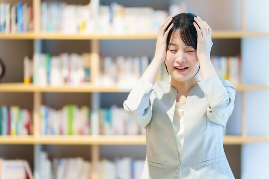 本棚の前に立つ頭を抱えた女性　作家　小説家　エッセイスト