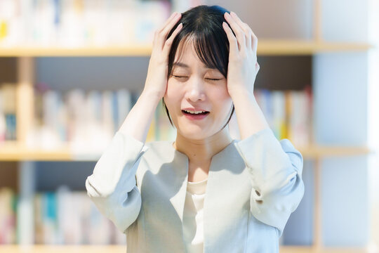 本棚の前に立つ頭を抱えた女性　作家　小説家　エッセイスト