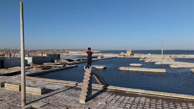 Visitor balances atop a ruined structure in Villa Epecu&eacute;n, Buenos Aires, Argentina, overlooking flooded remains of the former resort town destroyed by the 1985 inundation, drone pullback shot.