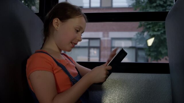 A laughing student girl on school bus with tablet