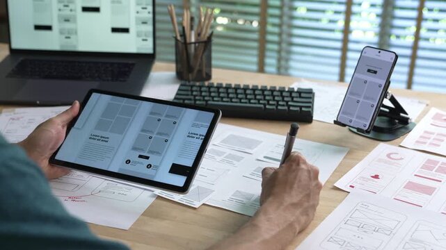 UX UI designer working on wireframes for a website and mobile app prototype, surrounded by sketches of user-flow and design tools, in concept of website and mobile application design concept.