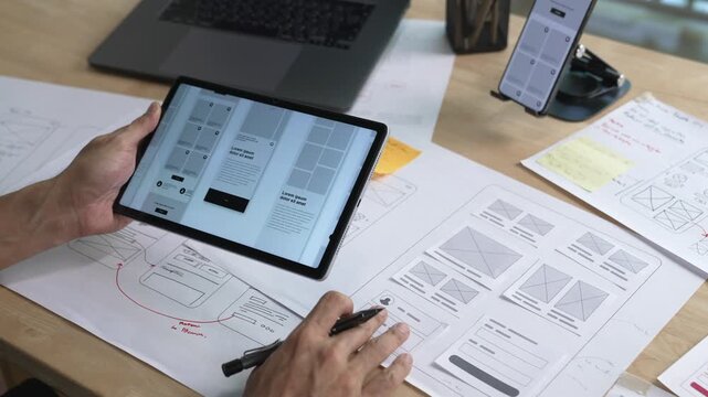 UX UI designer working on wireframes for a website and mobile app prototype, surrounded by sketches of user-flow and design tools, in concept of website and mobile application design concept.