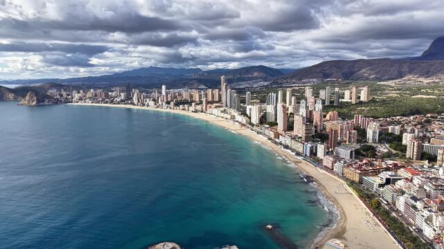 Aerial City Beach Beneath Mountain Backdrop, Turquoise Bay Curving Past Dense Highrises And Leafy Hills