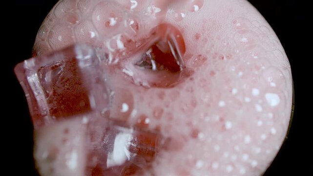 A close-up of red energy drink with ice cubes and bubbling foam captured in a vivid macro shot.