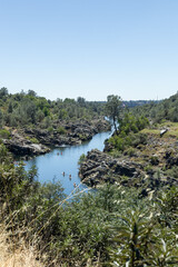 Fototapeta premium View of a river surrounded by rocks and trees with people swimming on a sunny day
