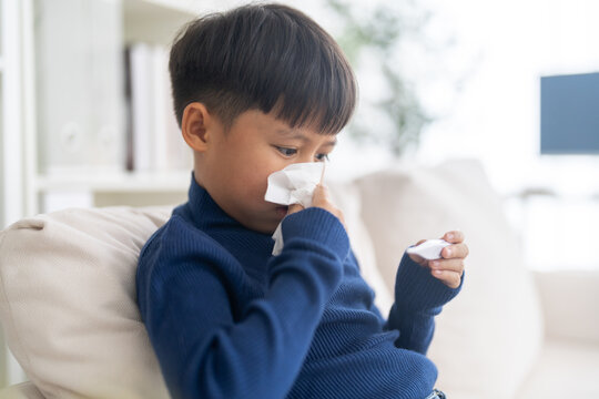 Sick asian boy child wiping runny nose with tissue and checking a digital thermometer for high fever temperature, Concept of flu symptoms, child health care, rsv, influenza and bronchitis illness