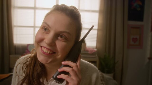 Caucasian teenager talking on retro cordless phone, smiling and gossiping while chatting with friend. Ideal for nostalgic 90s themed marketing, vintage technology ads, or youth lifestyle storytelling