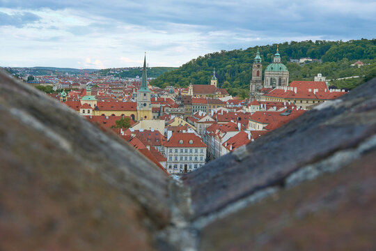 Scenic view of Prague Lesser Town (Mala Strana) with red rooftops and St. Nicholas Church dome, framed by a blurred stone wall in the foreground