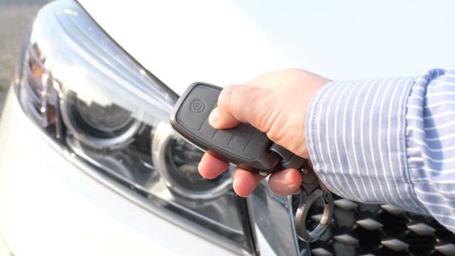 A woman's hand holds a car key against the background of headlight and presses the on off button.