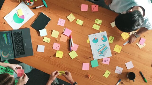 Top down aerial view of business team brainstorming idea and writing plan at colorful sticky notes. Professional project manager planning strategy while stick paper at meeting table. Convocation.