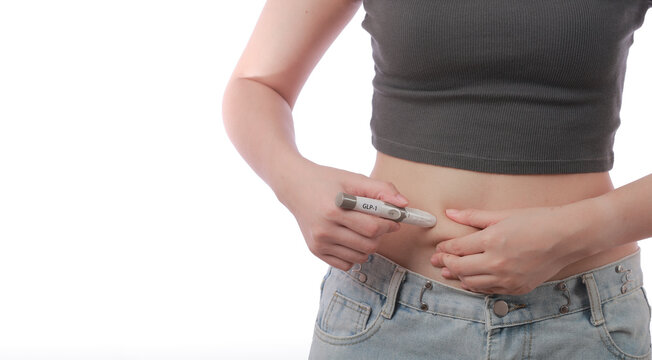 Focused woman performs GLP1 injection on her abdomen belly skin using pen device for healthy weight loss journey showing determined expression during home medical care treatment