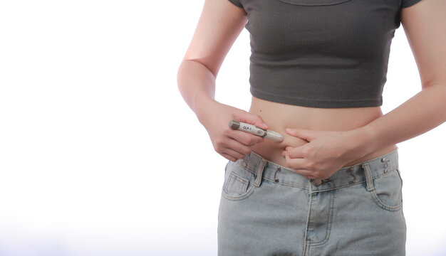 Determined young woman performs GLP1 injection on her abdomen belly skin using pen device for healthy weight loss journey showing determined expression during home medical care treatment