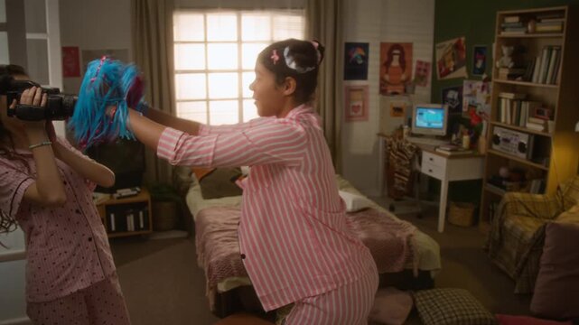 Caucasian teenage girl filming African American friend dancing with pom-poms using vintage camcorder during pajama party. Clip is ideal for youth lifestyle marketing and retro technology campaigns
