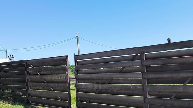 Rough-hewn wooden rural fencing reinforced with steel rods under clear blue sky, bottom-up perspective, aged timber texture, ideal for overlay and backdrops.
