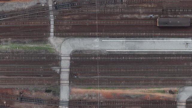 An overhead drone shot captures the complex parallel geometry of railway tracks and a train station platform in rural Hungary.