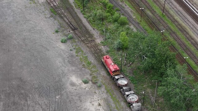Multiple railroad tracks run parallel through a green industrial landscape under an overcast sky.