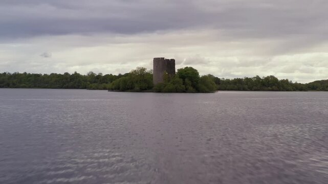 Fast aerial dolly skimming over water rushing towards centered Cloughoughter Castle island with striking foreground motion and compelling composition
