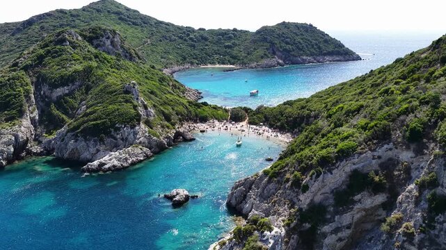 Drone view of Porto Timoni double beach in Corfu Greece. Scenic twin bays with crystal clear turquoise water, green lush hills, rocky coast and tourists sunbathing on summer holiday