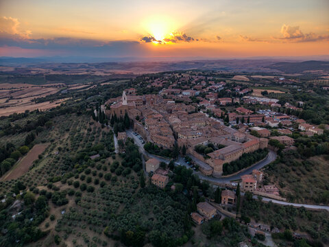 Aerial view of the historic town of Pienza at sunset, featuring terracotta rooftops, stone buildings, and surrounding olive groves in the landscape of Pienza, Tuscany, Italy.