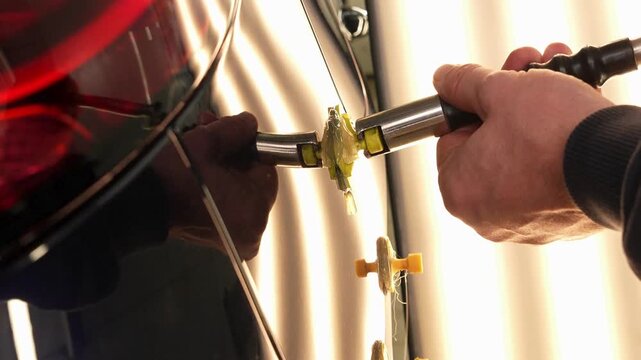 mechanic using precise tools to adjust and pull out dents in a cars rear side professional repair shop.