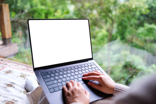 Mockup image of a woman working and typing on laptop computer with blank desktop white screen on the bed at home