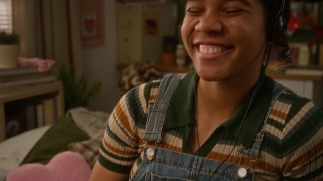 African American teenage girl holding vintage portable CD player, listening to music through headphones and smiling while singing along in bedroom. Retro technology commercial, youth lifestyle content