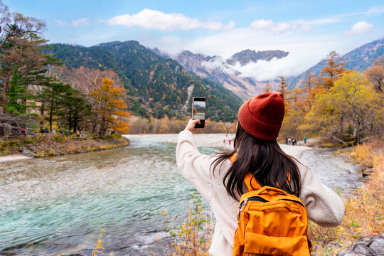 Young female tourist enjoying and taking a photo with beautiful autumn at kamikochi in Japan