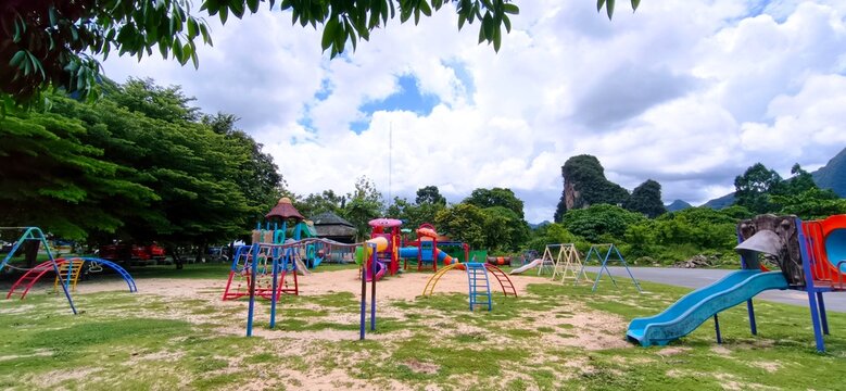 Colorful outdoor playground equipment on grass field with a scenic limestone mountain and cloudy sky background.