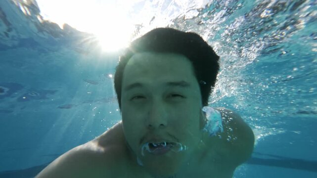 Underwater Selfie POV View of Southeast Asian Man Submerging in Swimming Pool with Air Bubbles