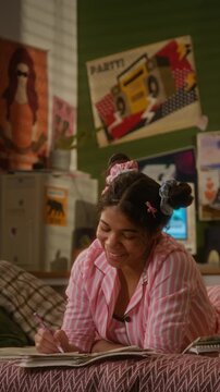 Vertical of African American teenage girl in pink pajamas lying on bed, thinking and writing in diary or journal. Educational apps, youth lifestyle, or back to school marketing campaigns
