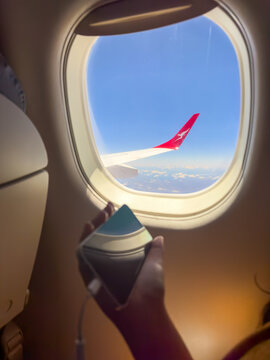 NEW SOUTH WALES, AUSTRALIA - DECEMBER 1 2024: A passenger uses a device to watch content in a Qantas plane with wing tips flying over Australia with clear blue skies