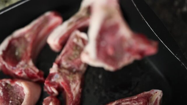 arranging and handling raw lamb chops on a dark surface in a neutral top-down perspective for food preparation and culinary arts use cases with red and white colors.
