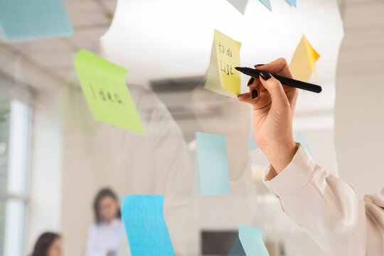 Person writing to do list on sticky note in office