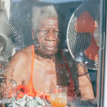 Elderly Black woman at an apartment window during a heatwave, feeling the stifling heat through the glass for climate change and health awareness themes