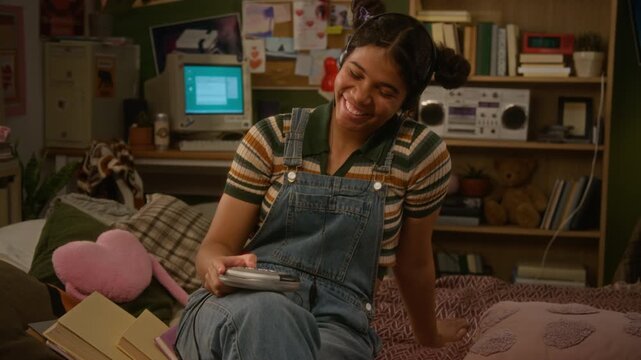 Teenage African American girl wearing headphones, holding retro CD player and smiling while enjoying favorite music in bedroom. Nostalgic marketing campaigns and youth lifestyle commercials