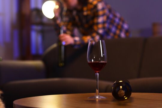 Glass of red wine on table with person opening bottle in background